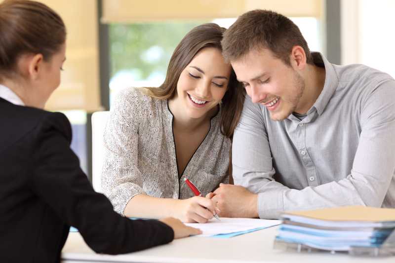 A happy young couple sign a document during a consultation with a solicitor