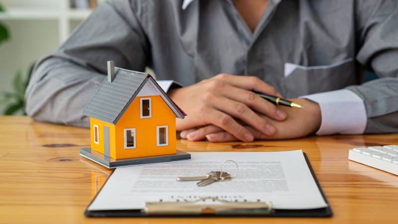 Purchasing Property A model of a house and house keys placed upon a property purchase contract.