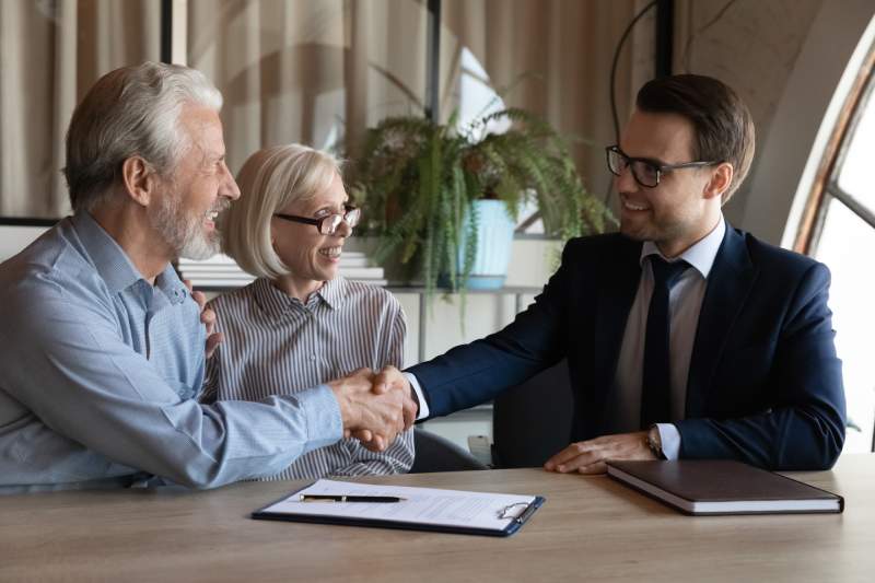 An elderly couple shake hands with a solicitor during a consultation