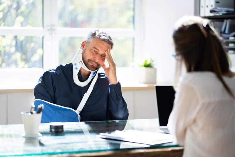 An injured man wearing a sling consults a solicitor about his injury