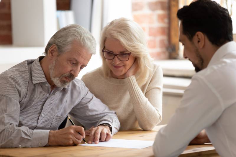 A happy senior couple sign a document during a power of attorney consultation with a solicitor