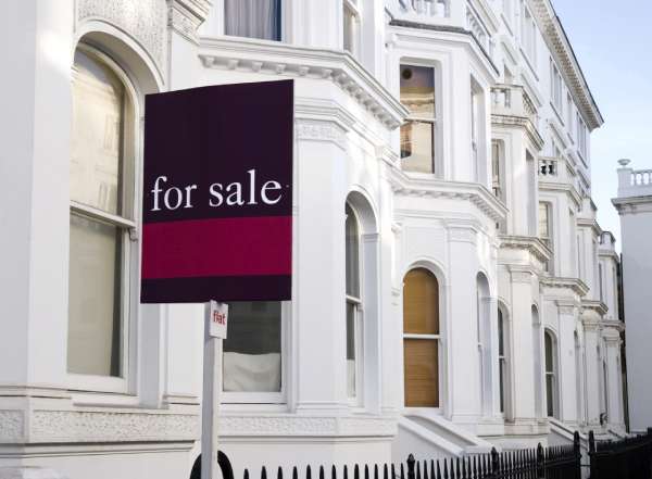 Traditional white terraced houses with a "for sale" sign out front