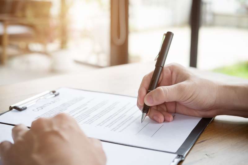 A closeup image of a man signing an employment contract in his home