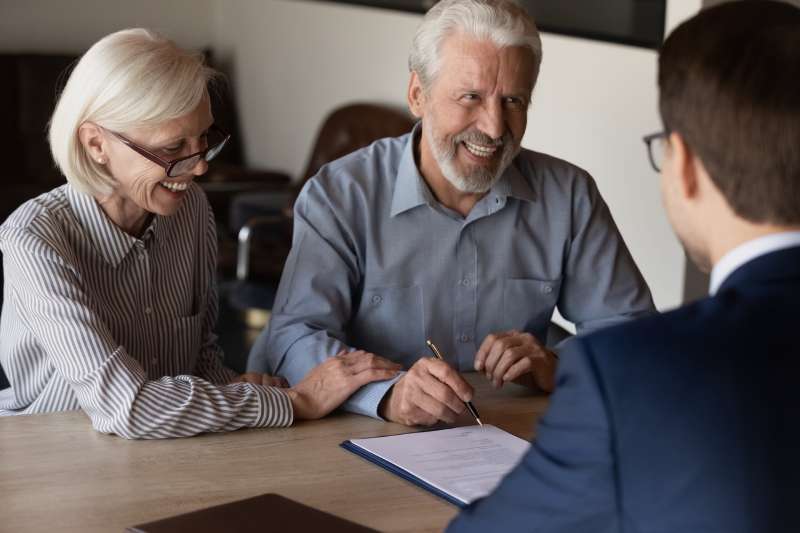 A cheerful elderly couple sign a document during a consultation with a solicitor